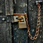 Schufa-Eintrag / Verrostete Kette und Vorhängeschloss an einer verwitterten, schwarz lackierten Holztür