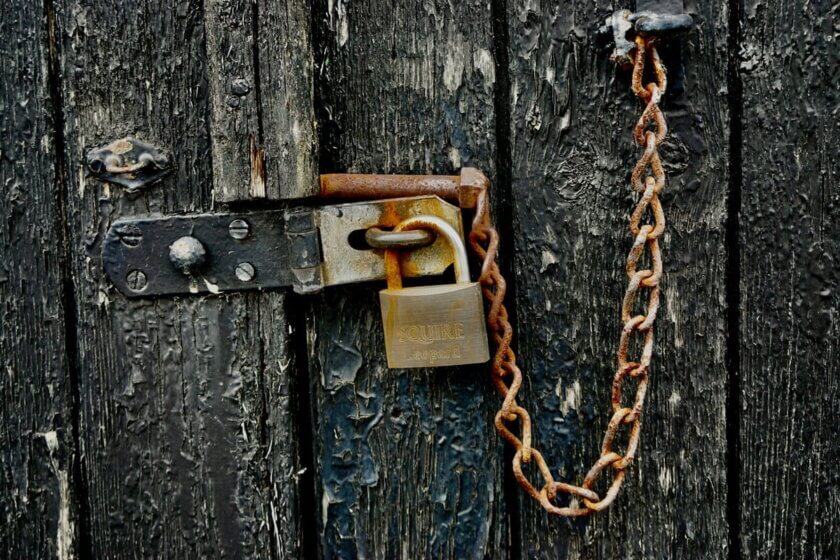 Schufa-Eintrag / Verrostete Kette und Vorhängeschloss an einer verwitterten, schwarz lackierten Holztür