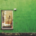 Greenwashing-Verbot / Grün gestrichene Hausfassade mit einem Fenster und abgeplatzter Farbe an der Wand