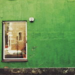 Greenwashing-Verbot / Grün gestrichene Hausfassade mit einem Fenster und abgeplatzter Farbe an der Wand