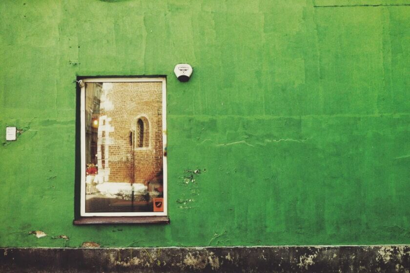 Greenwashing-Verbot / Grün gestrichene Hausfassade mit einem Fenster und abgeplatzter Farbe an der Wand